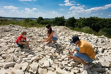 Eine Familie sucht an der Fossiliensammelstelle nach Versteinerungen. Alle drei knien mit Hammer und Meißel und versuchen die Platten zu teilen.