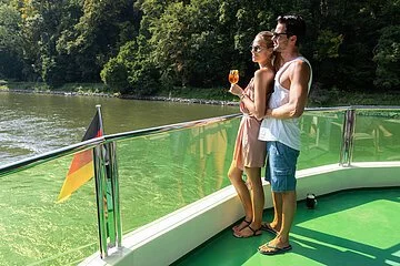 Eine Frau in sommerlicher Kleidung mit Eis in der Hand steht an der Reling. Sie ist an einen Mann hinter hier gelehnt. Beide genießen den Blick aufs Wasser. Eine Deutschlandfahne ist am Heck befestigt.