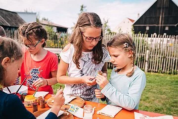 Vier Mädchen stehen an einem Biertisch im Garten des Jura-Bauernhof-Museums und basteln gemeinsam beim museumpädagischen Programm "ganz schön beeinDRUCKend".