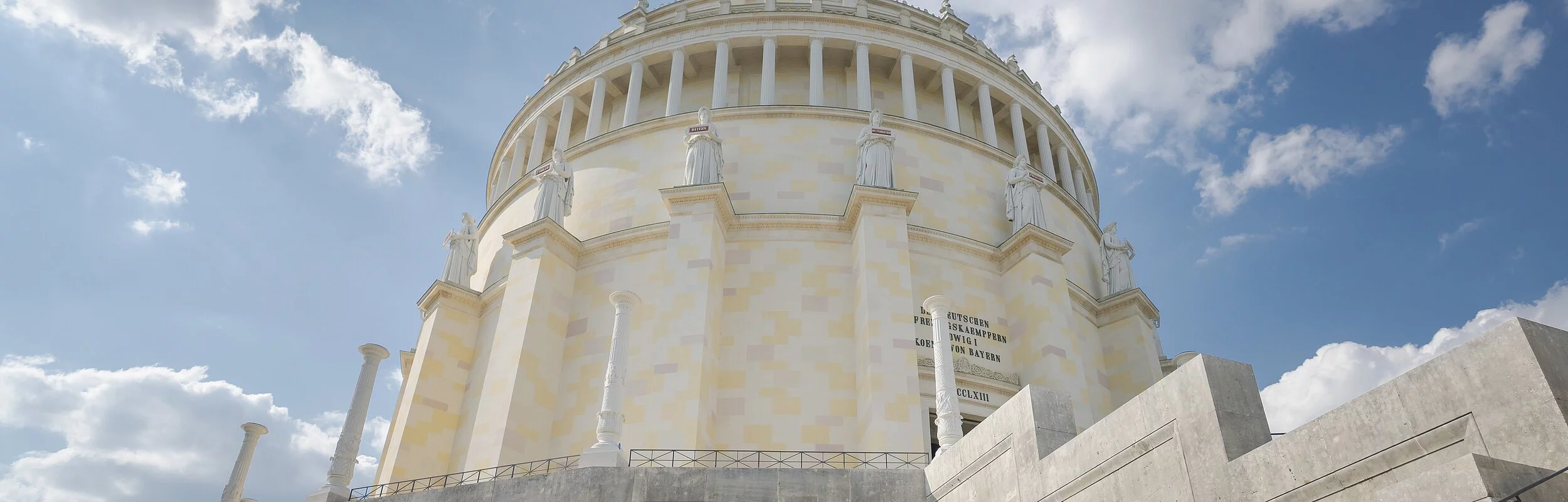 Der imposante Rundbau der Befreiungshalle auf dem Michelsberg. Rechts sind die Treppenstufen, die zu ihr hoch führen zu sehen. Der Himmel strahlt blau und ist leicht bedeckt.