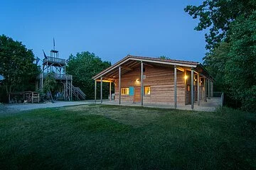 Internationaler Pfadfinderzeltplatz Bucher Berg Eine Holzhütte ist beleuchtet. Das Licht strahlt durch die Fenster nach außen. Links ist der Aussichtsturm im Dunkeln zu erkennen.
