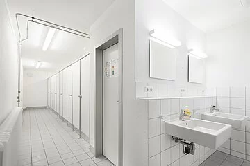 Der Waschraum ist komplett in weiß gehalten. Links ist ein langer Gang mit lauter Türen, die rechts zu Umkleiden und WC's führen.