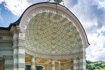 Auf dem Bild ist der mittlere und größte Pavillon des Hofgartens. Der Pavillon ist rund und nach vorne hin geöffnet. Ein Brunnen befindet sich im Zentrum. Dahinter stehen mehrere weiß, grau gemusterte Säulen. Die Kuppel ist innen mit einem mosaikartigen Muster aus grauen und weißen Elementen geschmückt. Das Dach wird von einer vasenähnlichen Figur geziert.
Bildbeschreibung ehemalige Kapuzinerkirche (innen)