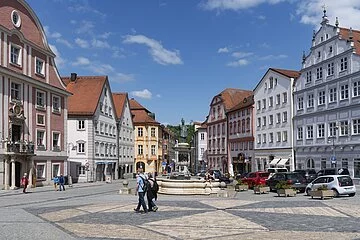 Zentrum des Bildes ist ein Brunnen aus Stein, auf dem die Statue des Hl. Willibalds thront. Neben dem Brunnen verlaufen zwei Häuserzeilen, die hinter dem Brunnen zusammenlaufen. Verschiedene Geschäfte und Cafés säumen die Straßen. Die Fassaden der Häuser sind in verschiedenen Farben gehalten. Der ganze Platz ist in dreiecksform angeordnet und mit Kopfsteinpflaster versehen.