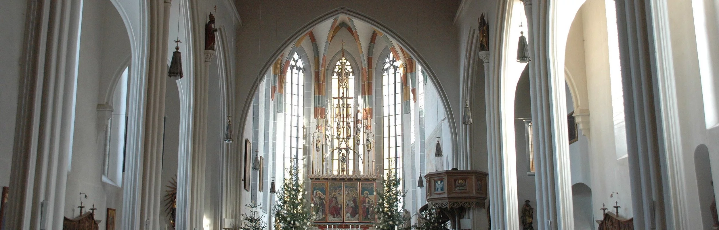 Blick in das lichtdurchflutete Innere mit dem Hauptaltar der von vier wegeschmückten Christbäumen umrahmt ist. Rechts vor dem Altar sieht man die Kanzel.