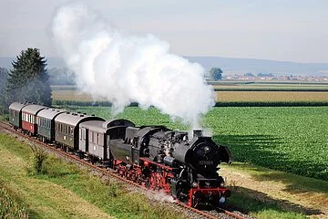 Eine Dampflokomotive mit Waggons fährt rauchend durch das Ries