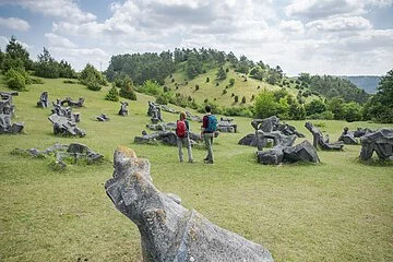 Auf den Wiesen im Hessental sind 78 überlebensgroße Plastiken, die zu einem fesselnden Mahnmal gegen Krieg und Gewalt geschaffen wurden, zu sehen. Inmitten dieses sind zwei Wanderer mit Rucksäcken unterwegs.
