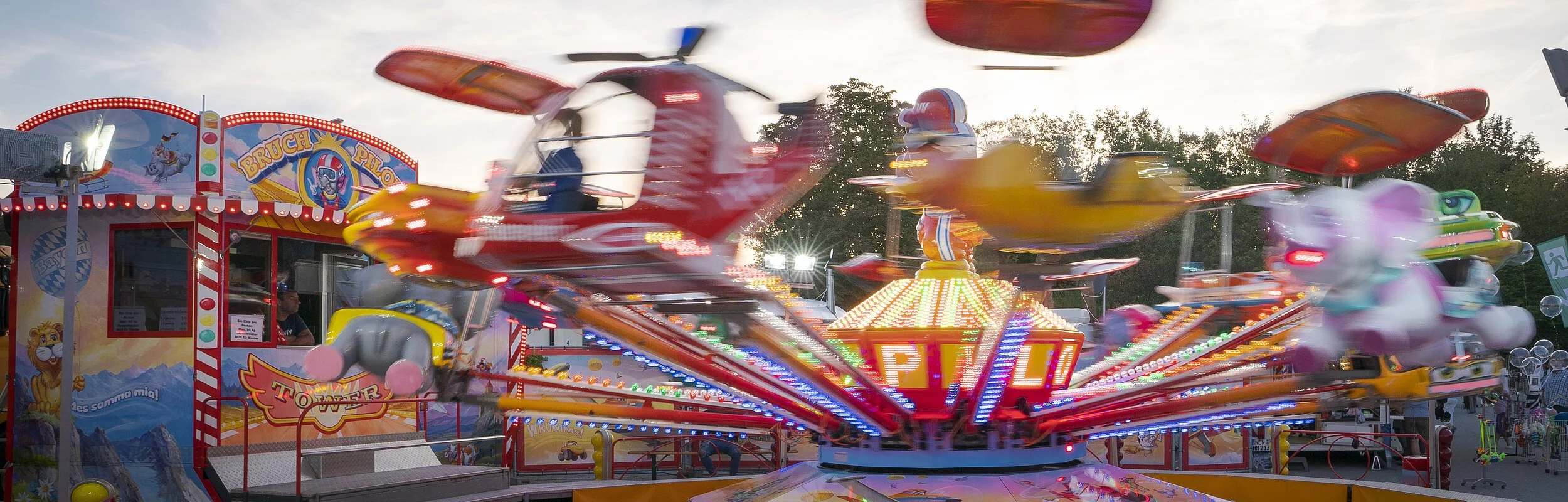 Ein farbenfrohes Fahrgeschäft auf dem Volksfest dreht sich recht schnell im Kreis. Dahinter sind weitere Buden zu erahnen.