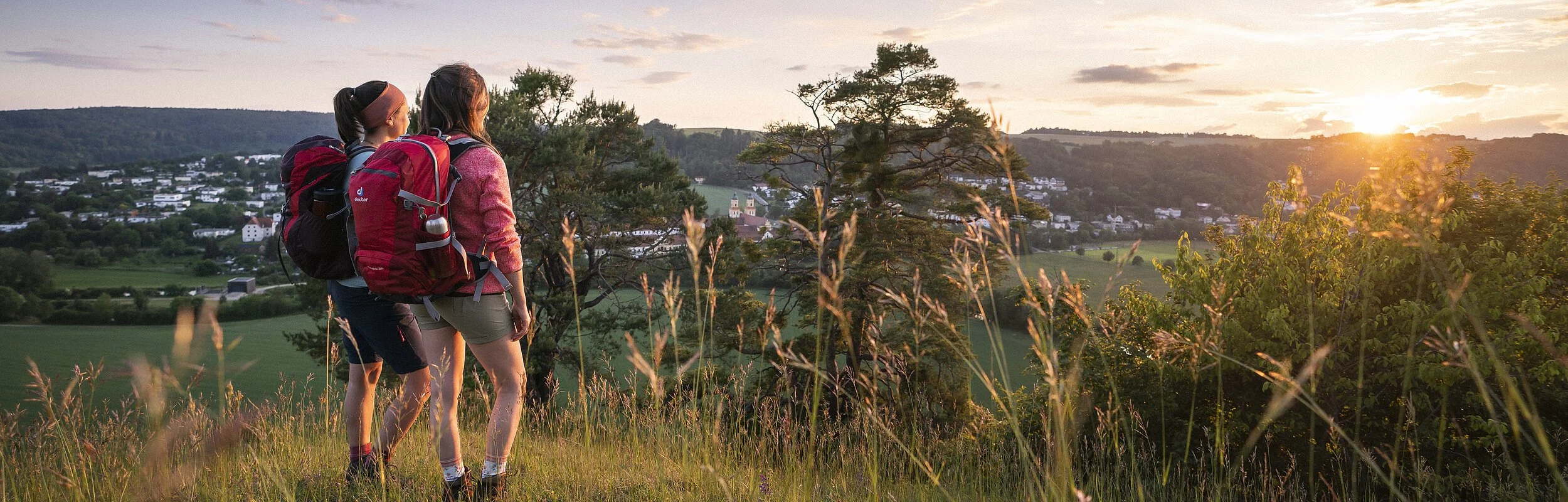 Zwei Frauen mit Wanderrucksäcken stehen am Frauenberg und genießen den Sonnenuntergang, sowie den schönen Blick über Eichstätt.