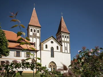 Kloster Heidenheim Das Kloster mit seinen zwei Türmen inmitten grüner Büsche. Der Himmel strahlt wolkenlos.