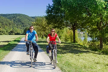 Altmühl - Radferien Tour 1-3 Zwei Radfahrer auf einem asphaltierten Radweg neben dem Fluss der Altmühl. Die Sonne strahlt und die zwei Radfahrer fahren gemütlich den Altmühltal-Radweg.