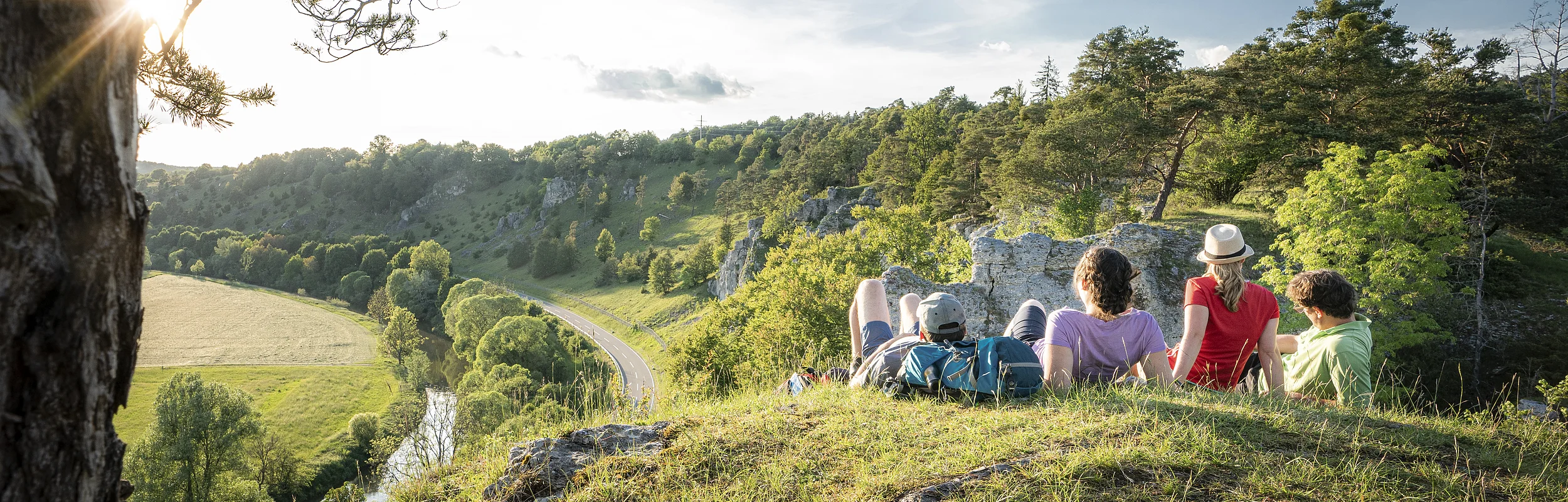Vier Wanderer liegen im grünen auf den 12 Aposteln am Altmühltal-Panoramaweg. Sie genießen den Sonnenuntergang und den Blick ins Tal.