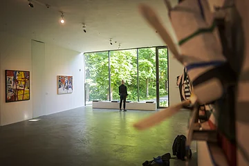 Ein Mann steht vor einer großen hellen Glaswand. Rechts und Links sind Exponate an der Wand zu erkennen.