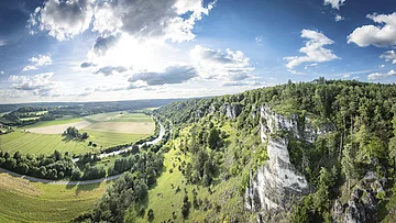 Arnsberger Leite mit Blick ins Altmühltal Weiter Blick ins Altmühltal: Rechts Felsen mit grünem Hang ins Tal und rechts sieht man den Fluss im Tal mit Wiesen.