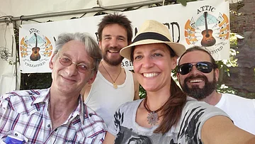 4 Personen machen ein Selfie. Ein Mann mit Brille und Karohemd, ein Mann mit Bart und weißem Top, eine Frau mit Strohhut und Pferdeschwanz und weiß/schwarz gemustertem Shirt, ein Mann mit Sonnenbrille und Bart und weißem T-Shirt.