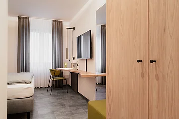 Das Zimmer ist simpel eingerichtet mit Holzschrank, Bett, Tisch, Stuhl und einem Fernseher.