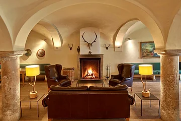 Aufenthaltsraum mit Deckengewölbe, Kamin, Sofa, Stühlen und gelben Lampen in rustikalem Stil.