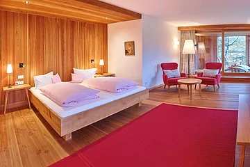 Ein Zimmer mit viel Holz, ausgestattet mit einem Doppelbett, roten Stühlen und einem roten Teppich.