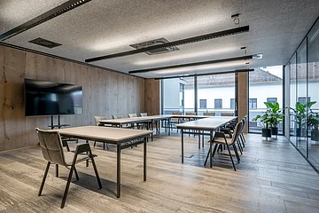 Die grauen Stühle sind um einen weißen langen Tisch ausgerichtet. Der Raum ist minimalistisch eingerichtet.