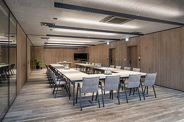 Der Raum ist in Naturtönen gestaltet, die grauen Stühle sind um die hellen Tische in U-Form ausgerichtet.