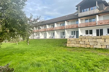 Das Gebäude mit Balkons und kleinen Terrassen ist umgeben von einer saftig grünen Wiese.