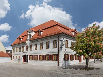 Ein gepflegtes Gebäude mit vielen Fenstern und weinroten Fensterläden.