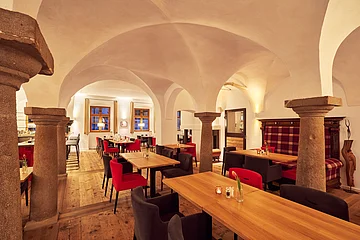 Der Speisesaal mit Gewölbe und Bögen ist mit Holzischen und roten/schwarzen Stühlen ausgestattet.