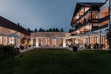 Hotel Eisvogel Außenansicht Außenansicht eines beleuchteten Gebäudekomplexes mit Terrasse und Garten bei Dämmerung.