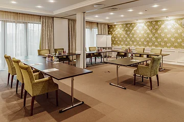 Tagungen Hotel Eisvogel Konferenzraum mit Tischen in U-Form, grünen Stühlen, Flipchart und Getränken auf den Tischen.