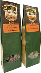 Zwei grüne Verpackungen mit Bio-Kürbiskernen, eine mit Schokolade, die andere gesalzen und geröstet.