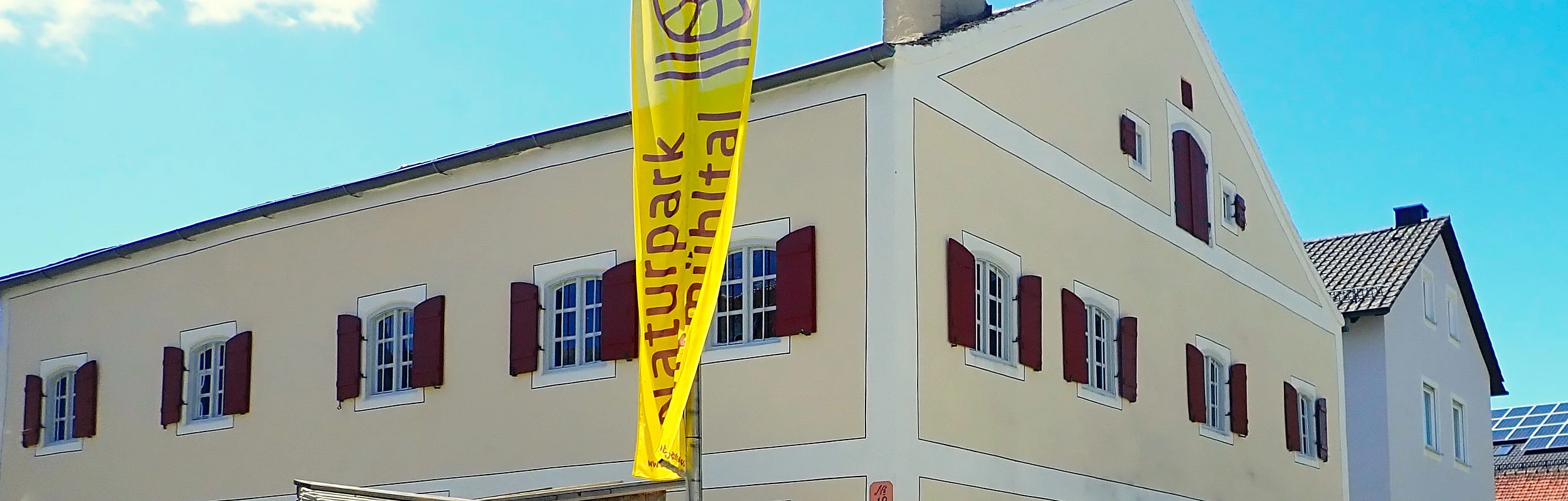 Gebäude mit gelber Flagge "Naturpark Altmühltal" und Schild "Jura-Bauernhof-Museum" davor.