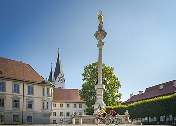 Gravelbiker am Residenzplatz Eichstätt Zwei Radfahrer fahren an einer Mariensäule auf einem Platz mit historischen Gebäuden vorbei.