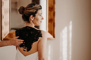 Person mit hochgestecktem Haar bekommt eine schwarze Paste auf den Rücken aufgetragen.