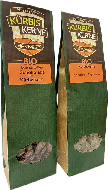 Zwei grüne Verpackungen mit Bio-Kürbiskernen, eine mit Schokolade, die andere gesalzen und geröstet.