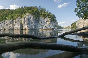 Fluss mit Felsen und Bäumen, Boot mit zwei Personen, Äste im Vordergrund im Wasser sichtbar