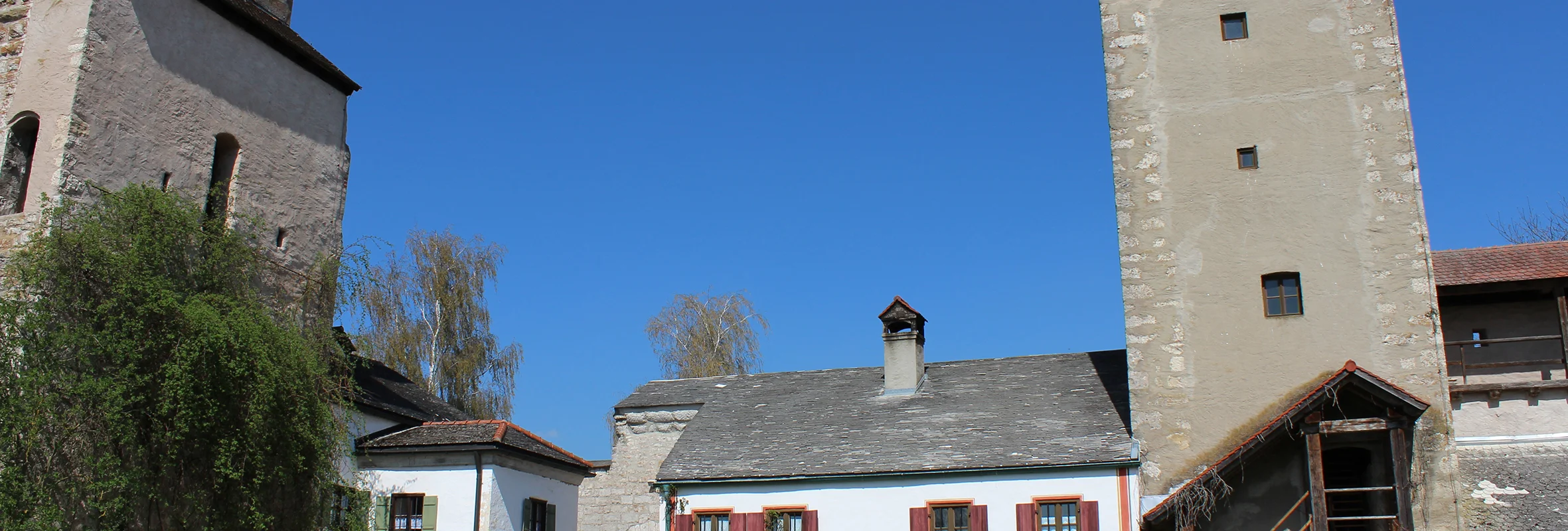 Bauernhof mit weißen Gebäuden, zwei Türmen und Gartenmöbeln unter blauem Himmel.