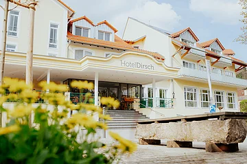 Eingangsbereich des Hotels Dirsch mit Stufen und gelben Blumen im Vordergrund bei Tageslicht.