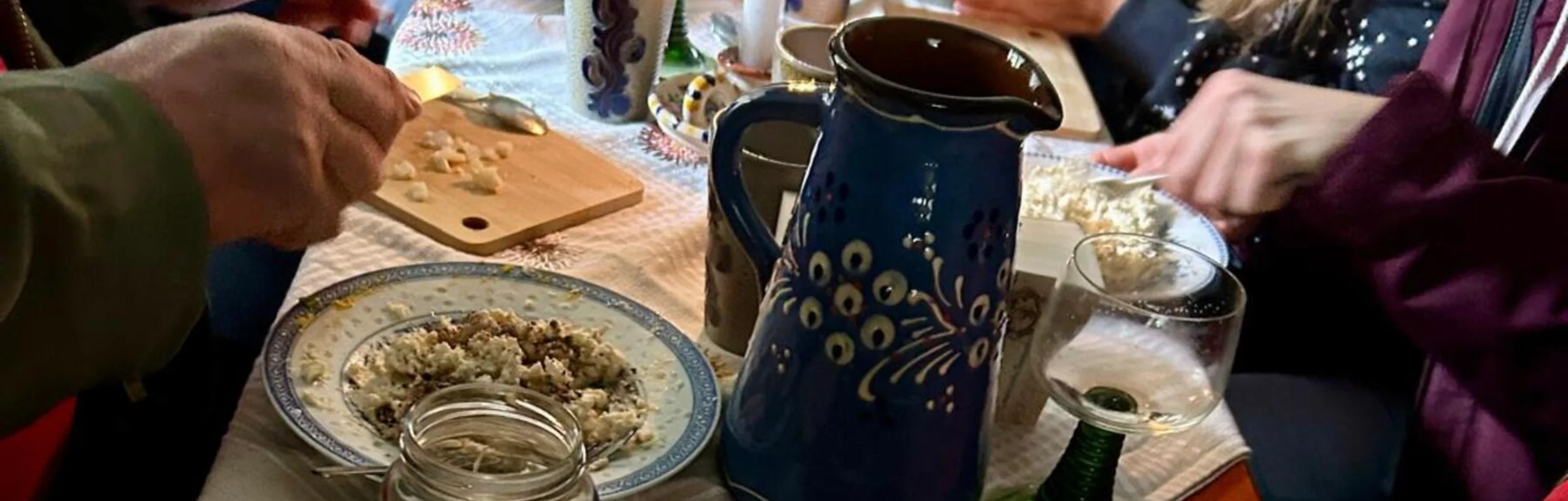 Menschen bereiten an einem gedeckten Tisch mit Kerze und Keramikgeschirr Speisen zu.