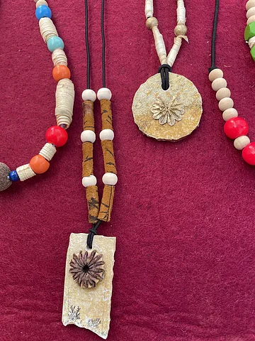 Nahaufnahme von handgefertigten Halsketten mit Naturstein- und Holzperlen auf rotem Stoff.