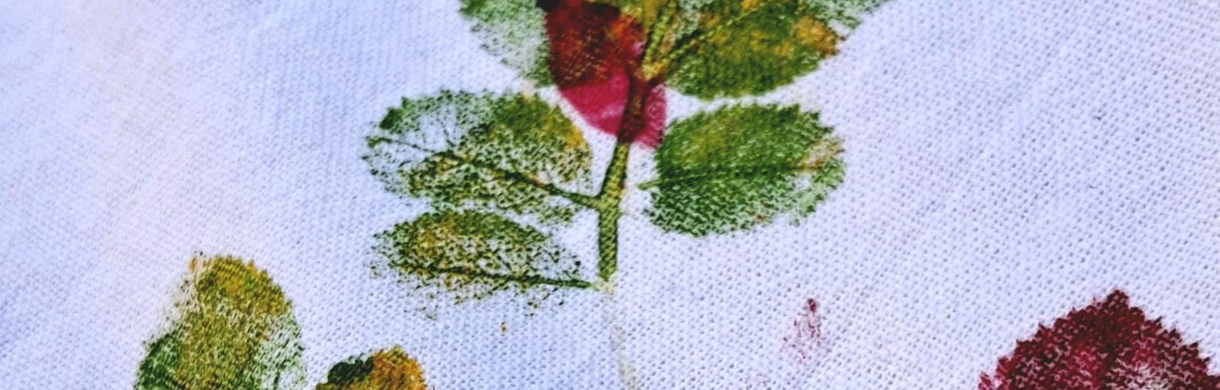 Druck von grünen und roten Blättern auf weißem Stoff mit sichtbarer Textur