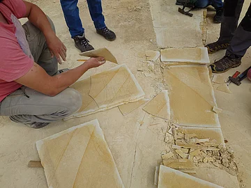Mehrere Personen bearbeiten und zerbrechen große, flache Steinplatten im Steinbruch.