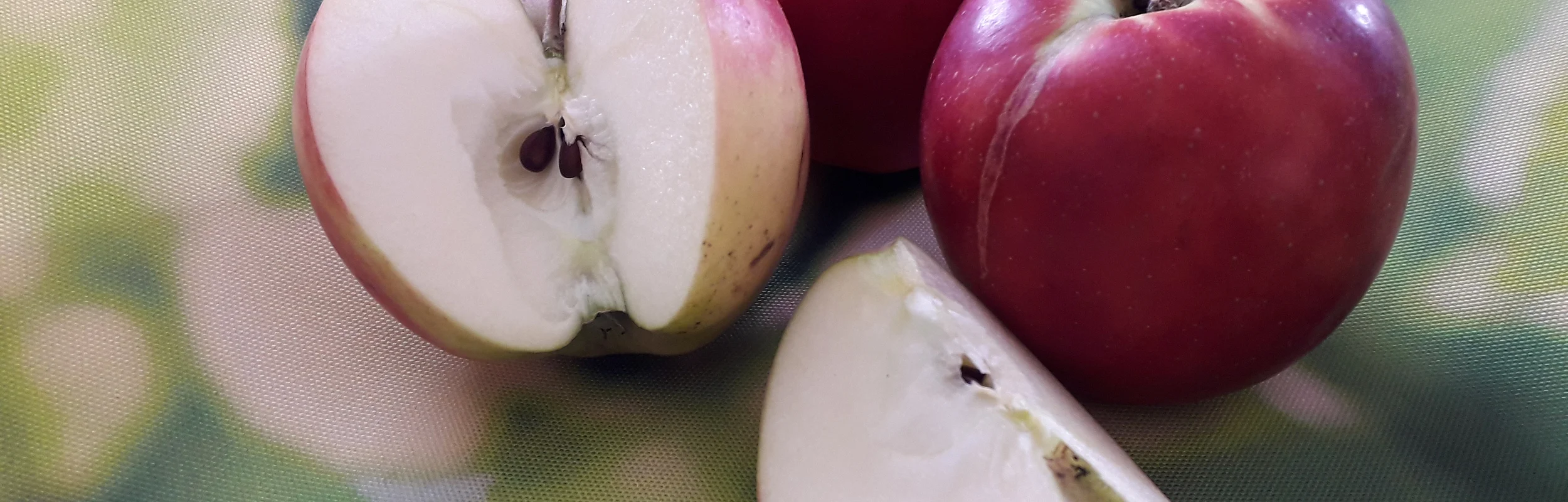 Zwei ganze rote Äpfel, ein halber und ein Viertel Apfel auf grünem unscharfem Hintergrund.