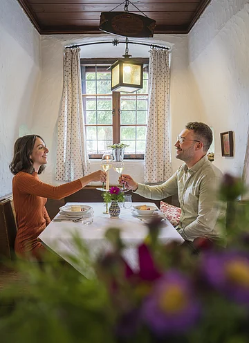 Ein Pärchen sitzt am gedeckten Tisch in der gemütlichen Gaststube des Restaurants "Zum Klosterbräu" in Bergen im Naturpark Altmühltal. Die beiden stoßen mit Weißwein an.