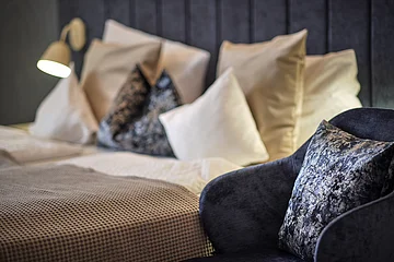 Bett mit mehreren Kissen und eine dunkelblaue Sitzgelegenheit mit gemustertem Kissen im Vordergrund.