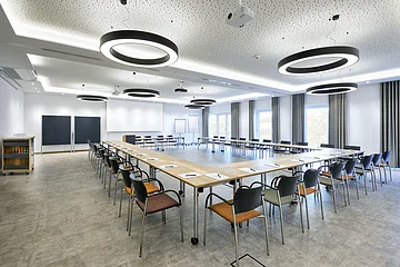Konferenzraum mit U-förmiger Tischanordnung, Stühlen, moderner Beleuchtung und Präsentationsflächen.