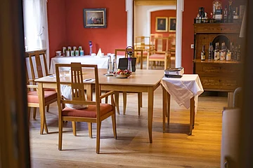 Holzstühle und Tisch in einem Raum mit roter Wand, darauf Wasserflaschen, Obstschale und ein Beamer.