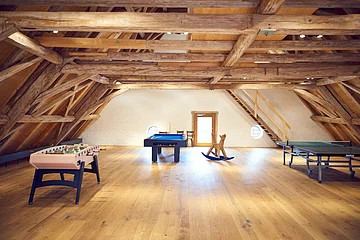 Spielecke im Dachgeschoss mit Tischfußball, Billard, Schaukelpferd und Tischtennisplatte unter Holzbalken.