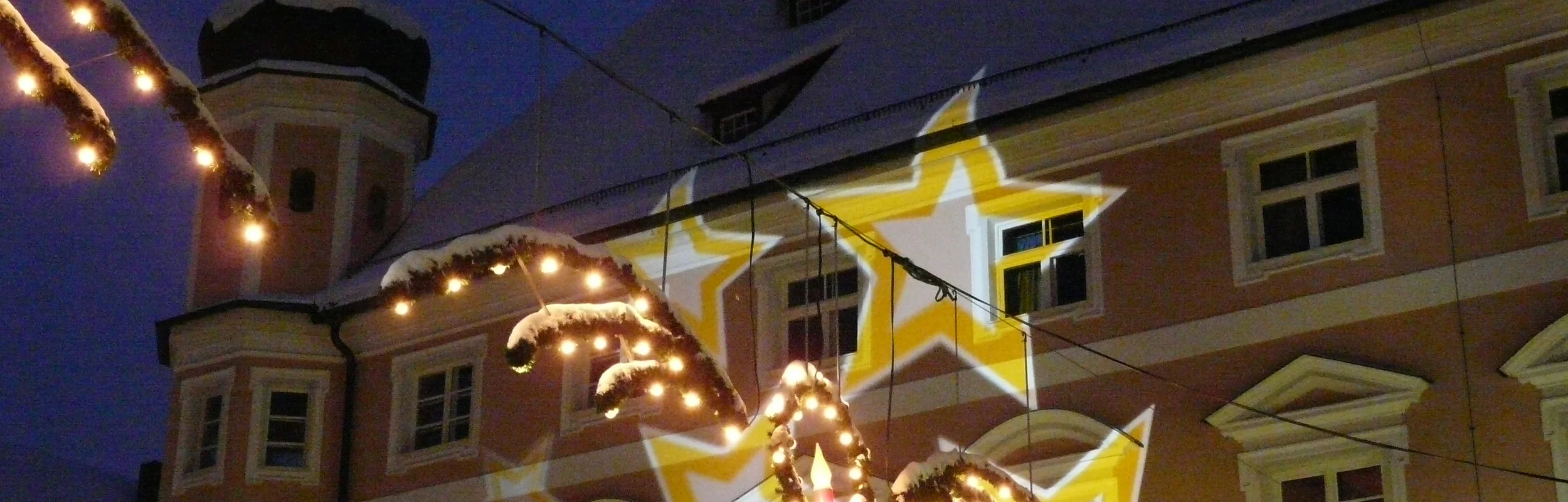 Beleuchtete Weihnachtsdekoration mit Lichterketten und Sternprojektionen an einem Gebäude bei Nacht im Winter.