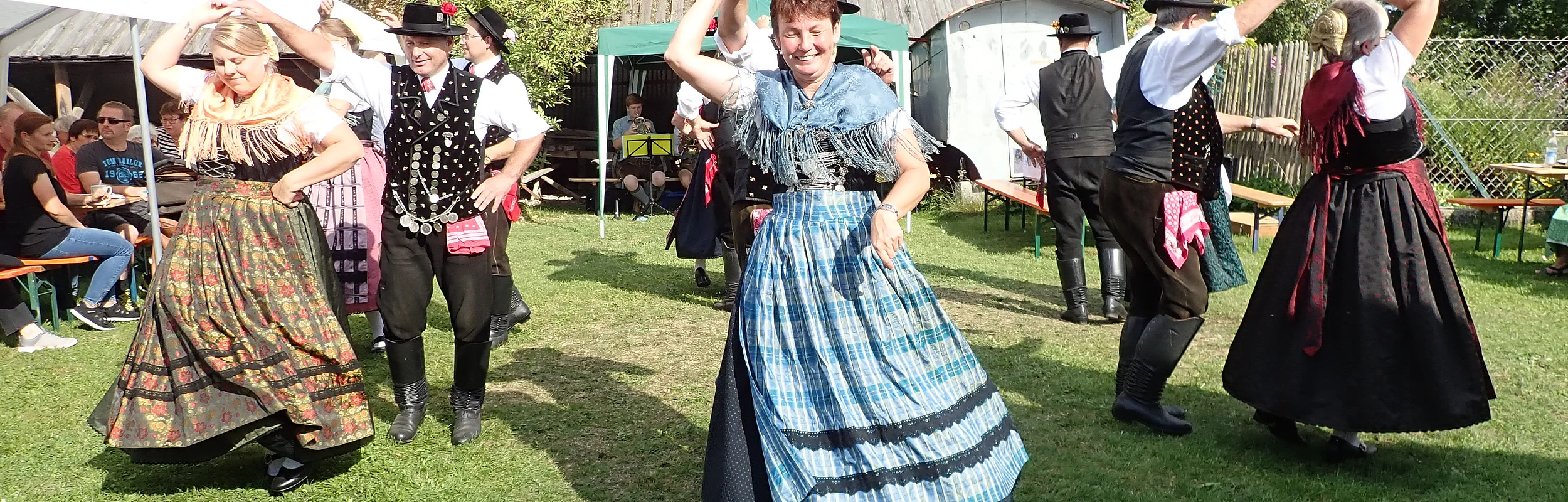 Drei Paare in Tracht tanzen im Garten des Jura-Bauernhof-Museum Hofstetten. Im Hintergrund ist ein Zelt und eine Scheune zu erahnen.