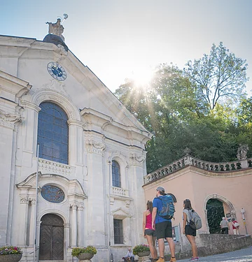 Zwei Frauen und ein Mann stehen vor der Kirche im Klosterinnenhof und bestaunen das Gebäude von außen.